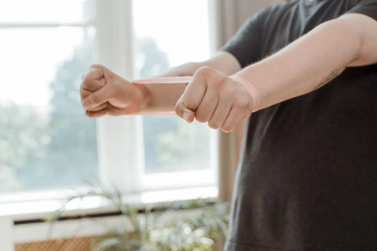A man performs arm exercises with a resistance band in a bright indoor space, highlighting sports therapy techniques.